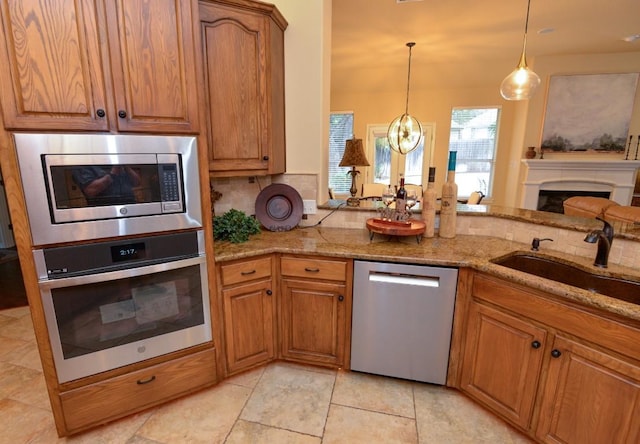 11409 Cezanne Ct, Austin, TX 78726 - kitchen featuring appliances with stainless steel finishes, a sink, brown cabinets, light stone counters, and a chandelier