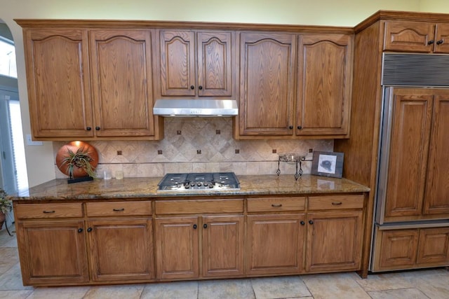 11409 Cezanne Ct, Austin, TX 78726 - kitchen with stainless steel gas stovetop, under cabinet range hood, paneled refrigerator, stone countertops, and brown cabinets
