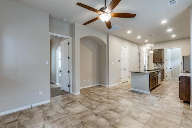 kitchen with dark brown cabinetry, sink, a center island with sink, ceiling fan, and decorative backsplash