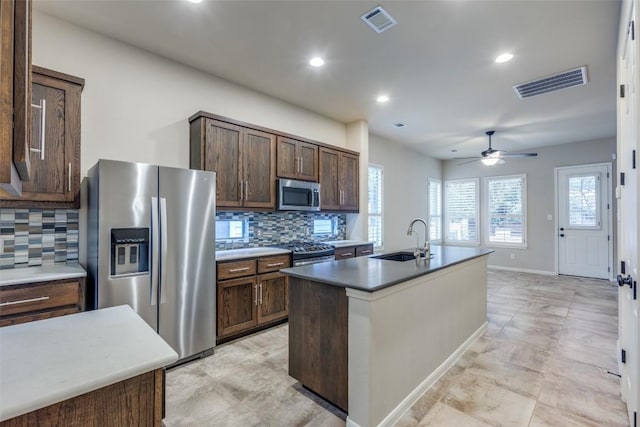 kitchen with stainless steel appliances, an island with sink, sink, and dark brown cabinetry