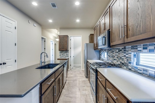 kitchen featuring appliances with stainless steel finishes, sink, a kitchen island with sink, and decorative backsplash