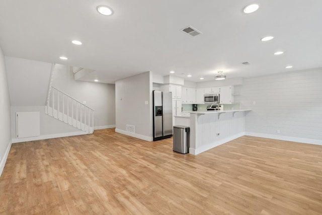 kitchen with appliances with stainless steel finishes, a kitchen breakfast bar, light hardwood / wood-style floors, white cabinets, and kitchen peninsula