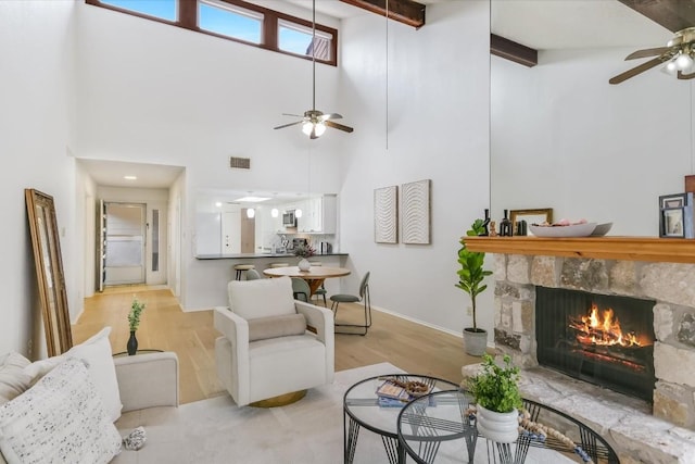 living room with beamed ceiling, ceiling fan, a stone fireplace, and light wood-type flooring