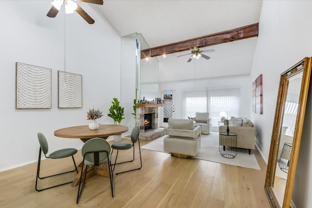 dining area featuring high vaulted ceiling, beamed ceiling, ceiling fan, a fireplace, and light hardwood / wood-style floors