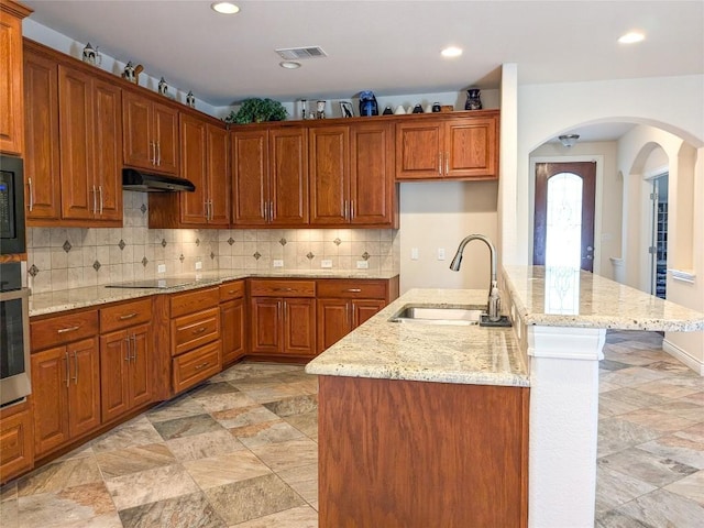 kitchen with visible vents, under cabinet range hood, arched walkways, black appliances, and a sink