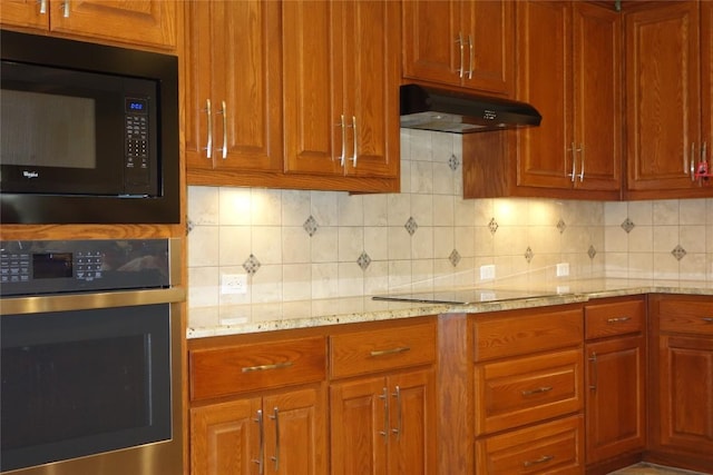 kitchen with light stone counters, brown cabinetry, black appliances, under cabinet range hood, and tasteful backsplash