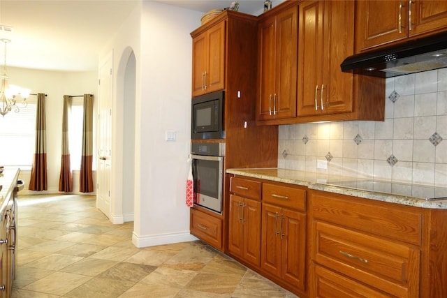 kitchen featuring light stone countertops, arched walkways, black appliances, under cabinet range hood, and backsplash