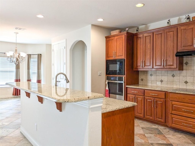 kitchen featuring visible vents, black appliances, light stone counters, backsplash, and a breakfast bar area