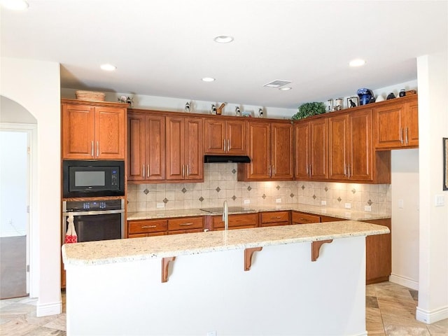 kitchen with visible vents, a kitchen bar, black appliances, under cabinet range hood, and backsplash