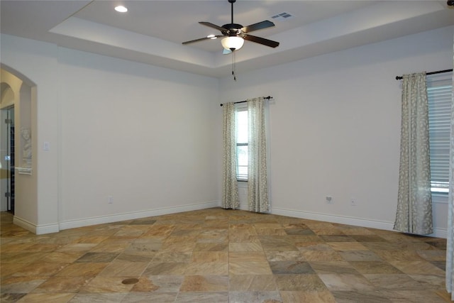 empty room with a ceiling fan, baseboards, visible vents, arched walkways, and a raised ceiling