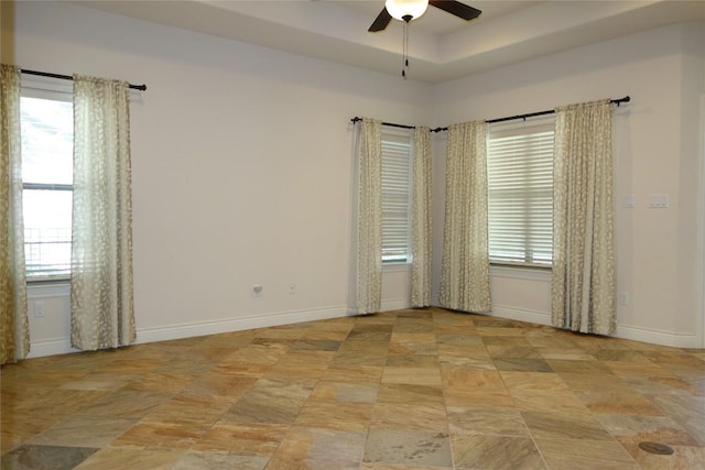 empty room featuring a tray ceiling, baseboards, plenty of natural light, and a ceiling fan