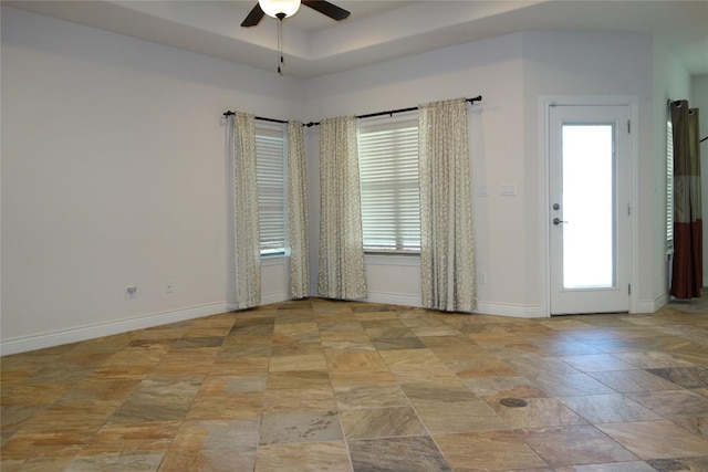 empty room featuring a raised ceiling, baseboards, and ceiling fan