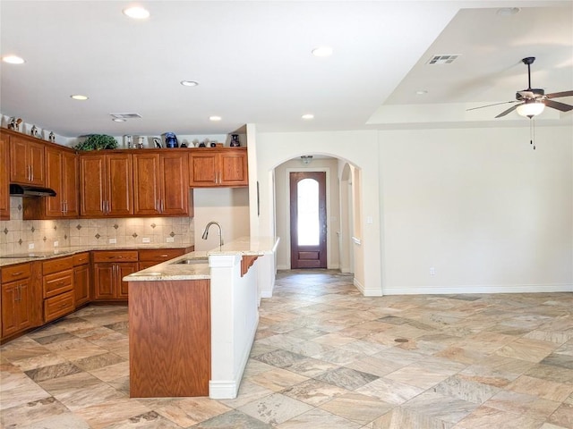 kitchen featuring visible vents, a sink, under cabinet range hood, backsplash, and black electric cooktop