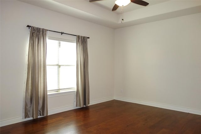 empty room with dark wood-type flooring, a ceiling fan, baseboards, and a raised ceiling