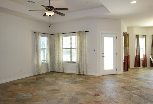 spare room with a ceiling fan, a tray ceiling, baseboards, and visible vents