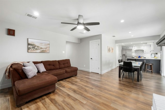 living room featuring ceiling fan, visible vents, baseboards, and light wood-type flooring