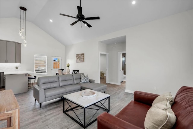 living area featuring ceiling fan, high vaulted ceiling, light wood-style flooring, and baseboards