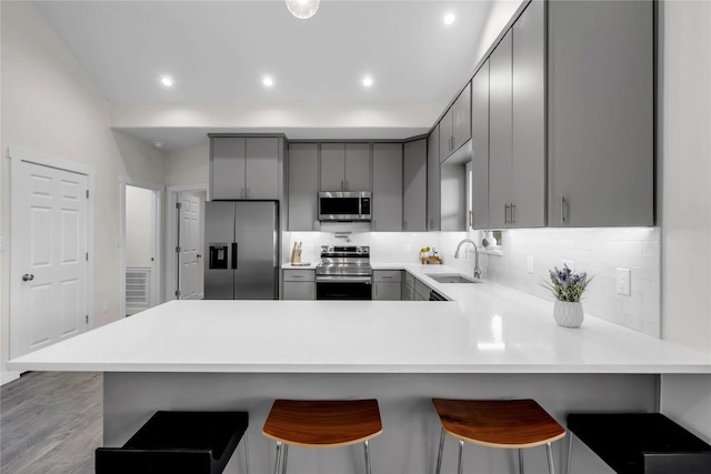 kitchen with a breakfast bar, gray cabinetry, appliances with stainless steel finishes, a sink, and a peninsula