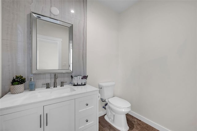 bathroom featuring toilet, decorative backsplash, vanity, wood finished floors, and baseboards