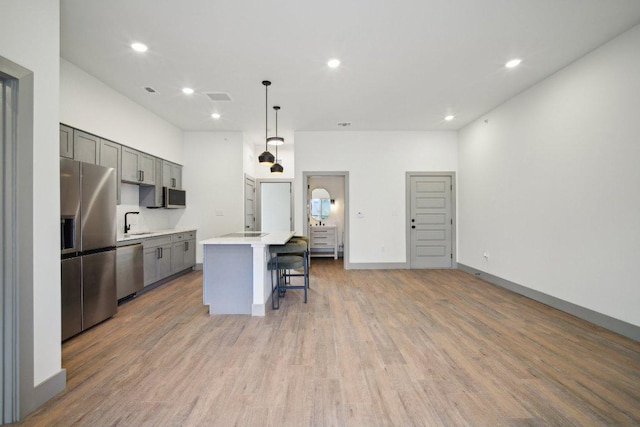 kitchen featuring stainless steel appliances, light countertops, gray cabinetry, light wood-type flooring, and a kitchen bar