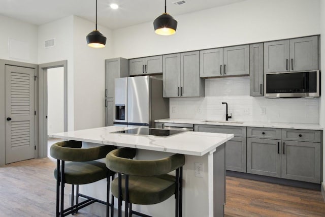 kitchen featuring gray cabinetry, stainless steel appliances, a sink, visible vents, and tasteful backsplash