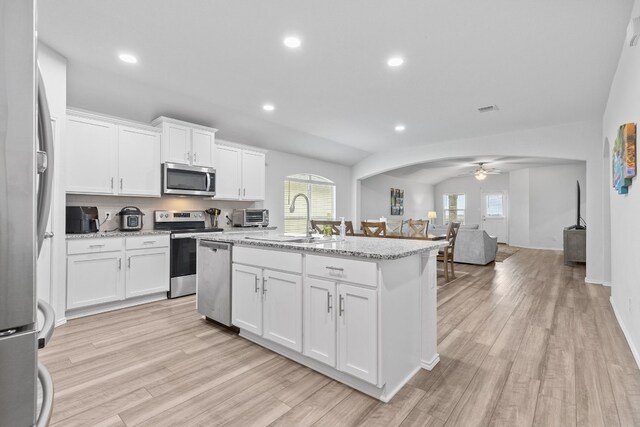 kitchen featuring appliances with stainless steel finishes, white cabinetry, sink, light stone counters, and a center island with sink