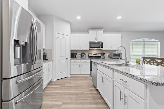 kitchen with appliances with stainless steel finishes, tasteful backsplash, white cabinets, light stone countertops, and light wood-type flooring