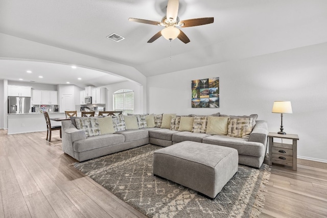 living room with ceiling fan, vaulted ceiling, and light wood-type flooring