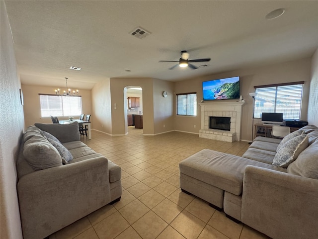 living room with a fireplace, ceiling fan with notable chandelier, a textured ceiling, and light tile patterned floors