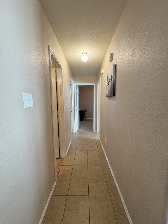 hallway with a textured ceiling and light tile patterned floors