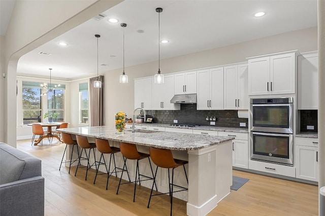 kitchen featuring a notable chandelier, under cabinet range hood, a sink, tasteful backsplash, and double oven