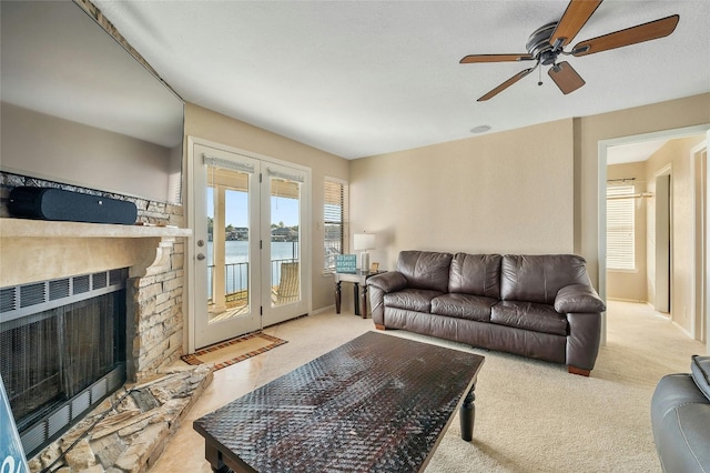 carpeted living area featuring a water view, a ceiling fan, a stone fireplace, and baseboards