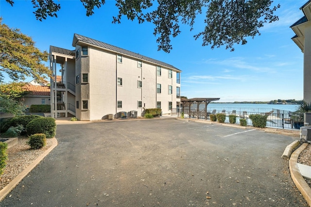 view of property with cooling unit, uncovered parking, a water view, and fence