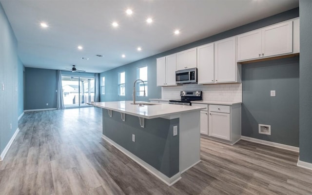 kitchen featuring an island with sink, light wood-style flooring, appliances with stainless steel finishes, open floor plan, and a sink