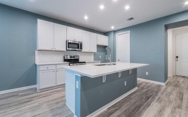 kitchen with tasteful backsplash, visible vents, an island with sink, stainless steel appliances, and a sink