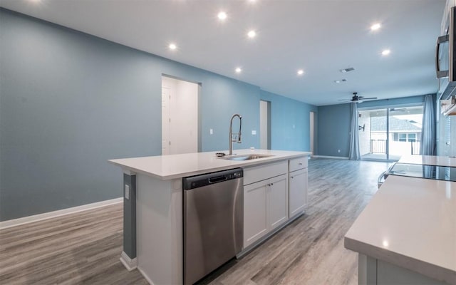 kitchen featuring a center island with sink, light wood finished floors, light countertops, stainless steel dishwasher, and a sink