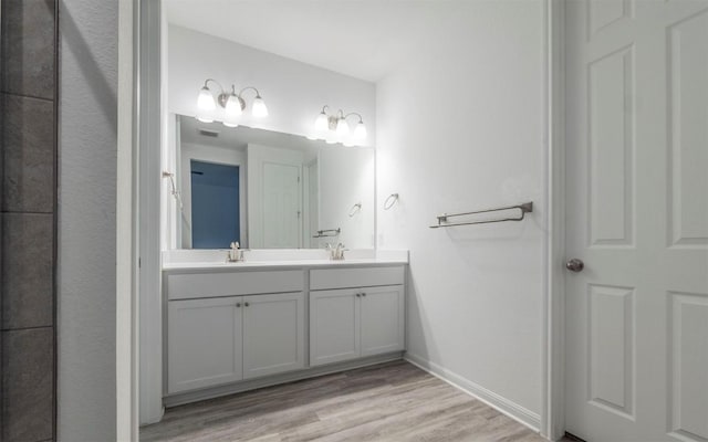 full bath featuring double vanity, wood finished floors, a sink, and baseboards