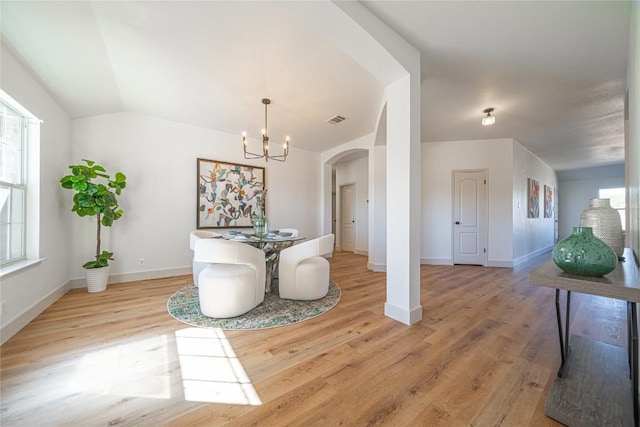 dining room with a notable chandelier, vaulted ceiling, and light wood-type flooring