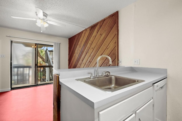 kitchen featuring wood walls, dishwasher, sink, white cabinets, and a textured ceiling