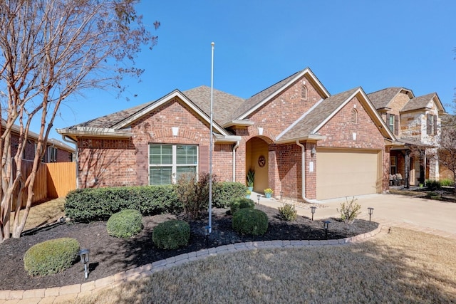 view of front of house with brick siding, driveway, an attached garage, and fence