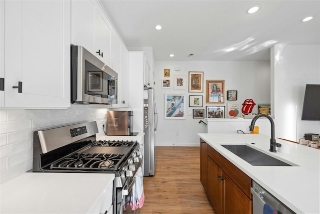 kitchen featuring tasteful backsplash, white cabinetry, sink, stainless steel appliances, and light hardwood / wood-style flooring