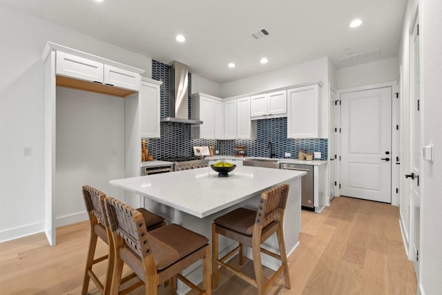 2707 Dulce Ln Unit 7, Austin, TX 78704 - kitchen with wall chimney exhaust hood, stainless steel dishwasher, light wood-style flooring, tasteful backsplash, and white cabinetry