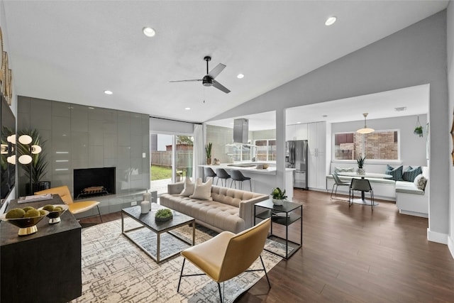 living room featuring vaulted ceiling, ceiling fan, a tiled fireplace, and hardwood / wood-style floors