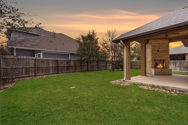 yard at dusk with a patio and an outdoor stone fireplace