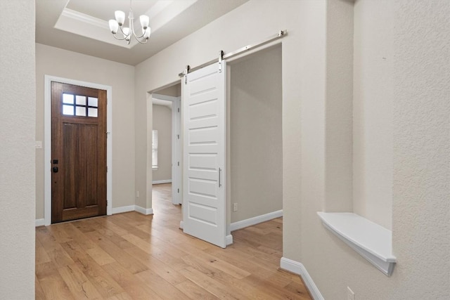 entryway featuring a tray ceiling, a barn door, a chandelier, and light wood-type flooring