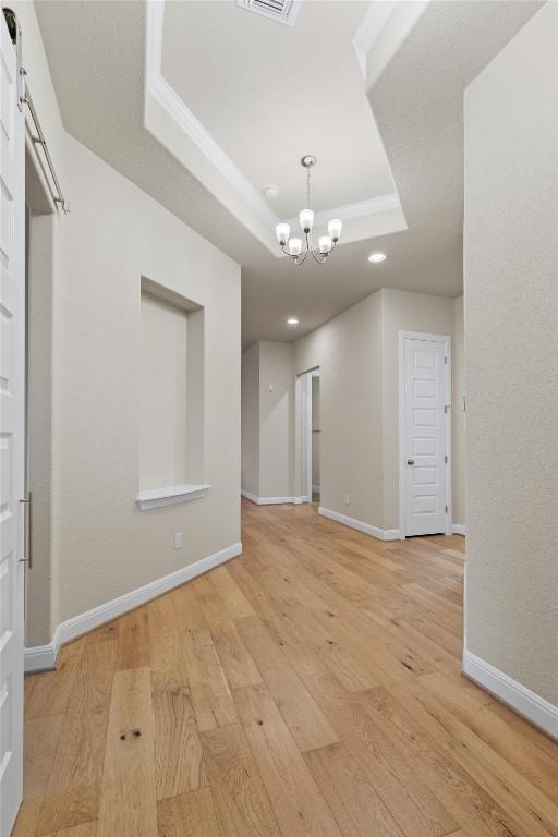 spare room with a chandelier, a barn door, a raised ceiling, and light hardwood / wood-style flooring