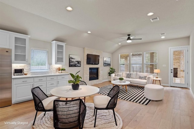 dining room with a fireplace, vaulted ceiling, ceiling fan, and light wood-type flooring