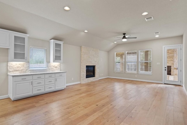 unfurnished living room with a stone fireplace, vaulted ceiling, light hardwood / wood-style floors, and ceiling fan