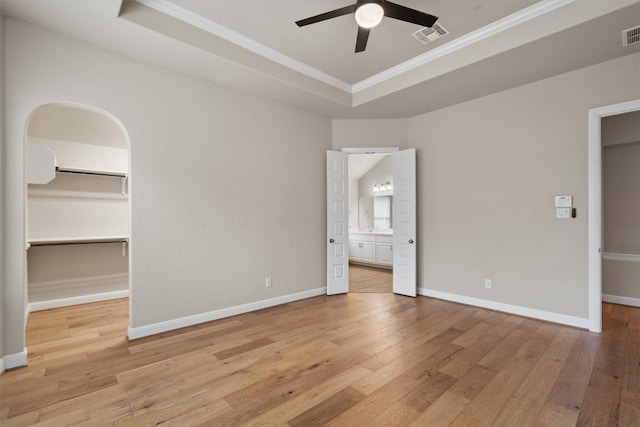 unfurnished bedroom featuring a tray ceiling, ornamental molding, light hardwood / wood-style floors, and a spacious closet