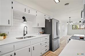 kitchen with sink, stainless steel fridge, tasteful backsplash, white cabinets, and decorative light fixtures